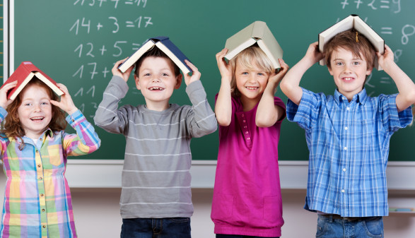 Kinder vor der Tafel mit Büchern am Kopf